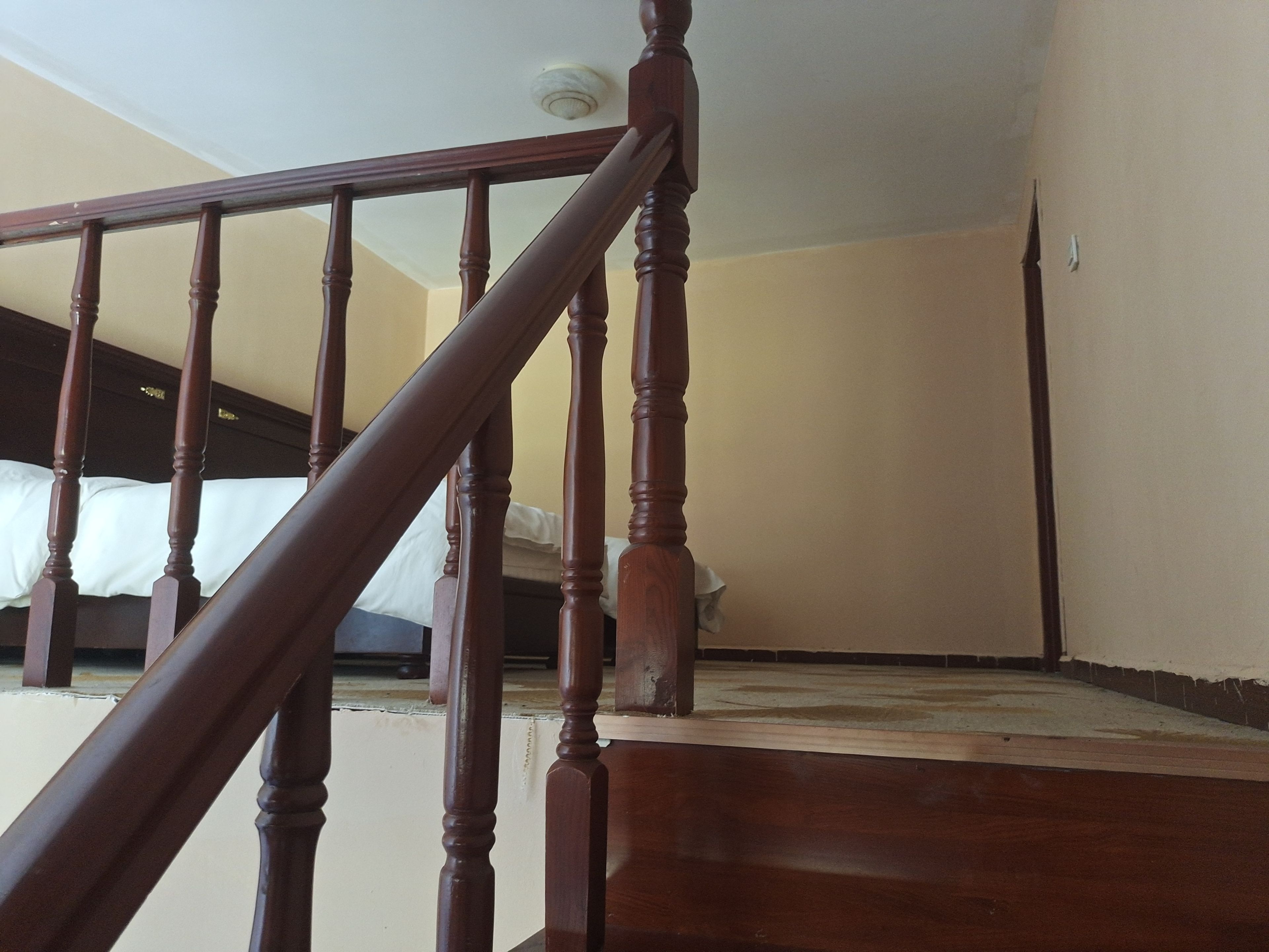 A wooden staircase with a handrail leading to a bedroom with a bed and a ceiling light.