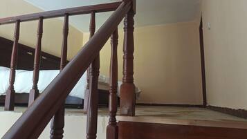 A wooden staircase with a handrail leading to a bedroom with a bed and a ceiling light.