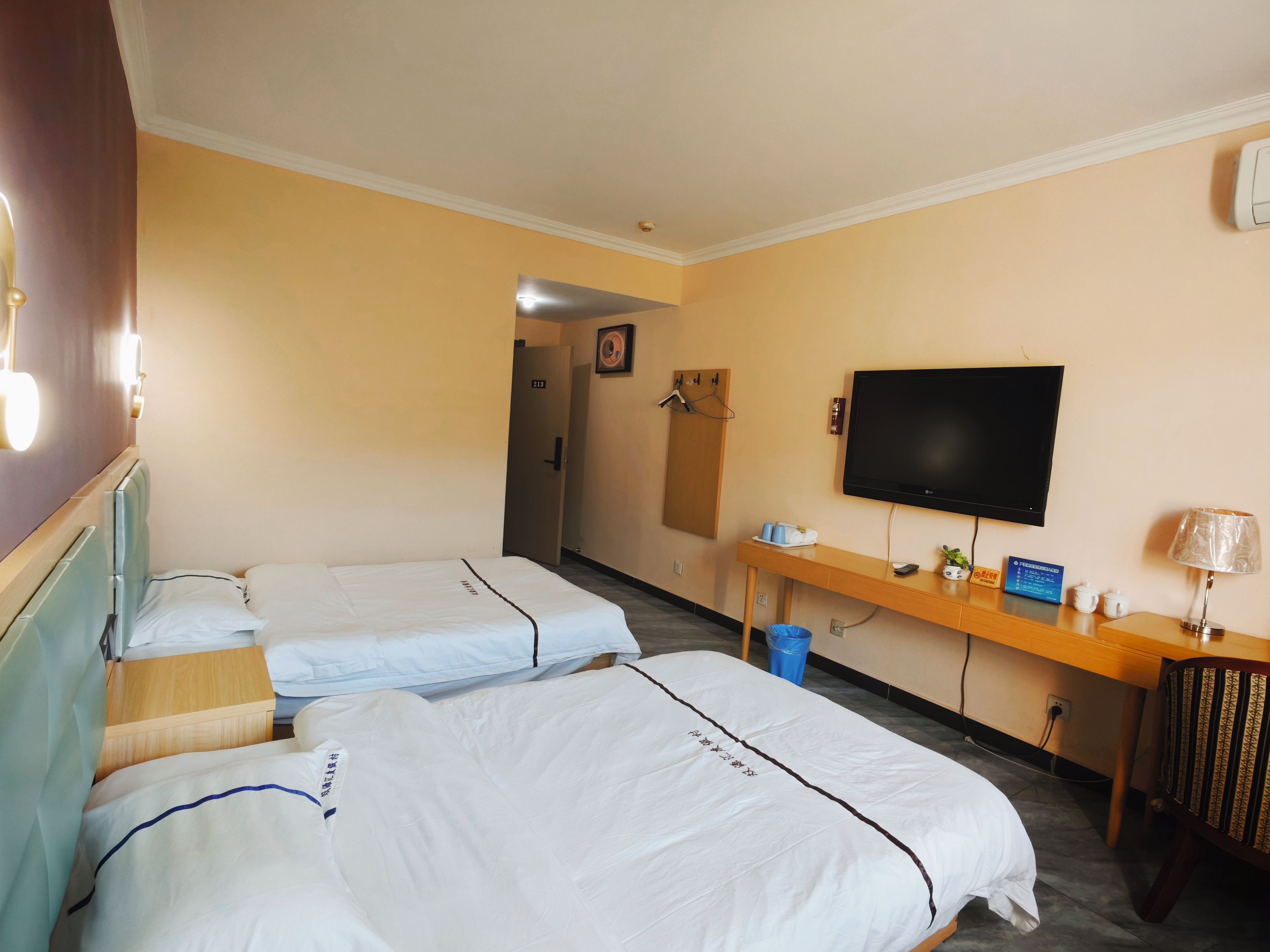Een hotelkamer met twee bedden, een televisie, een bureau met lamp en een televisie aan de muur.
