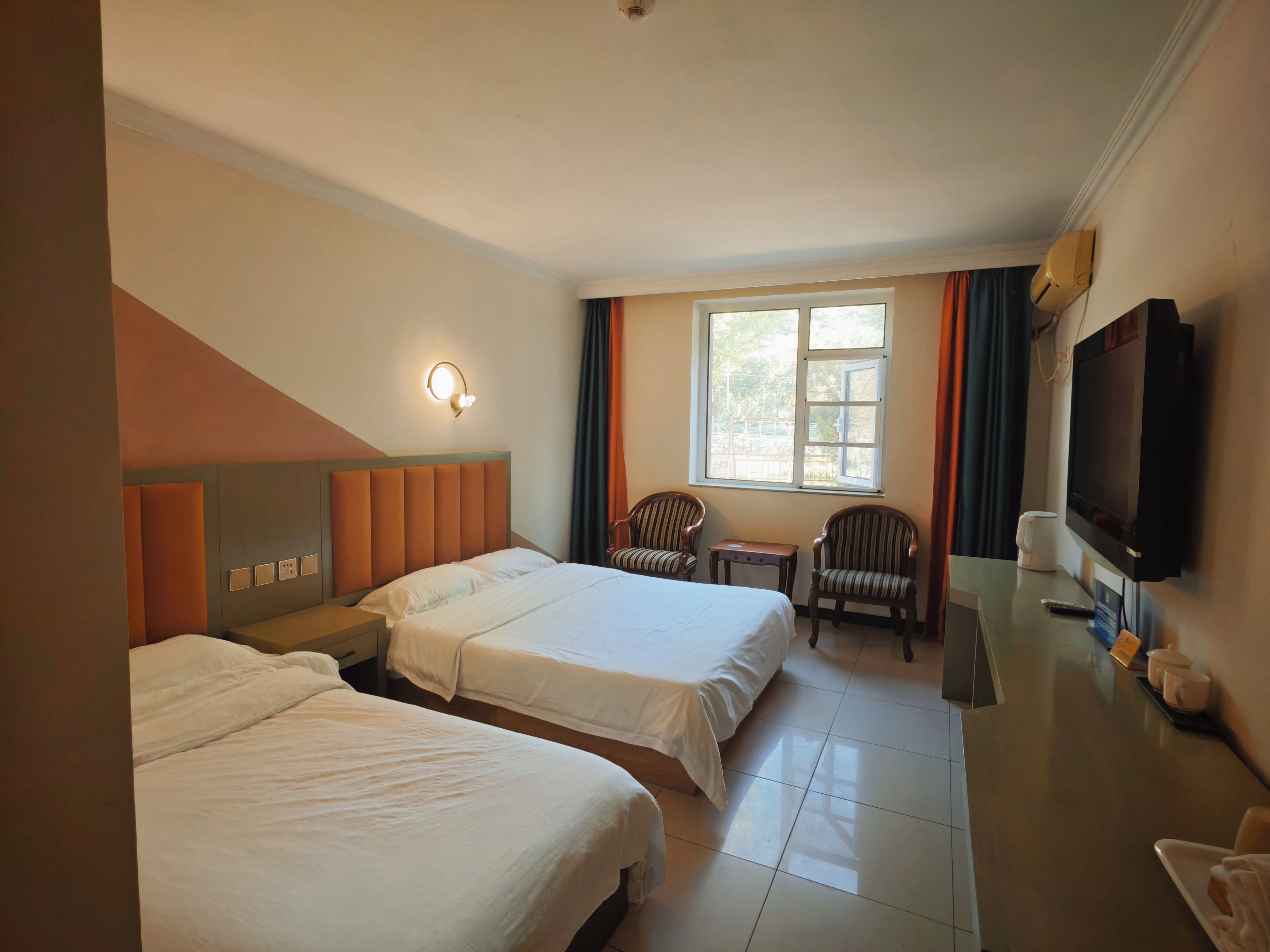 A hotel room with two beds, a television, a window with curtains, and a small table.