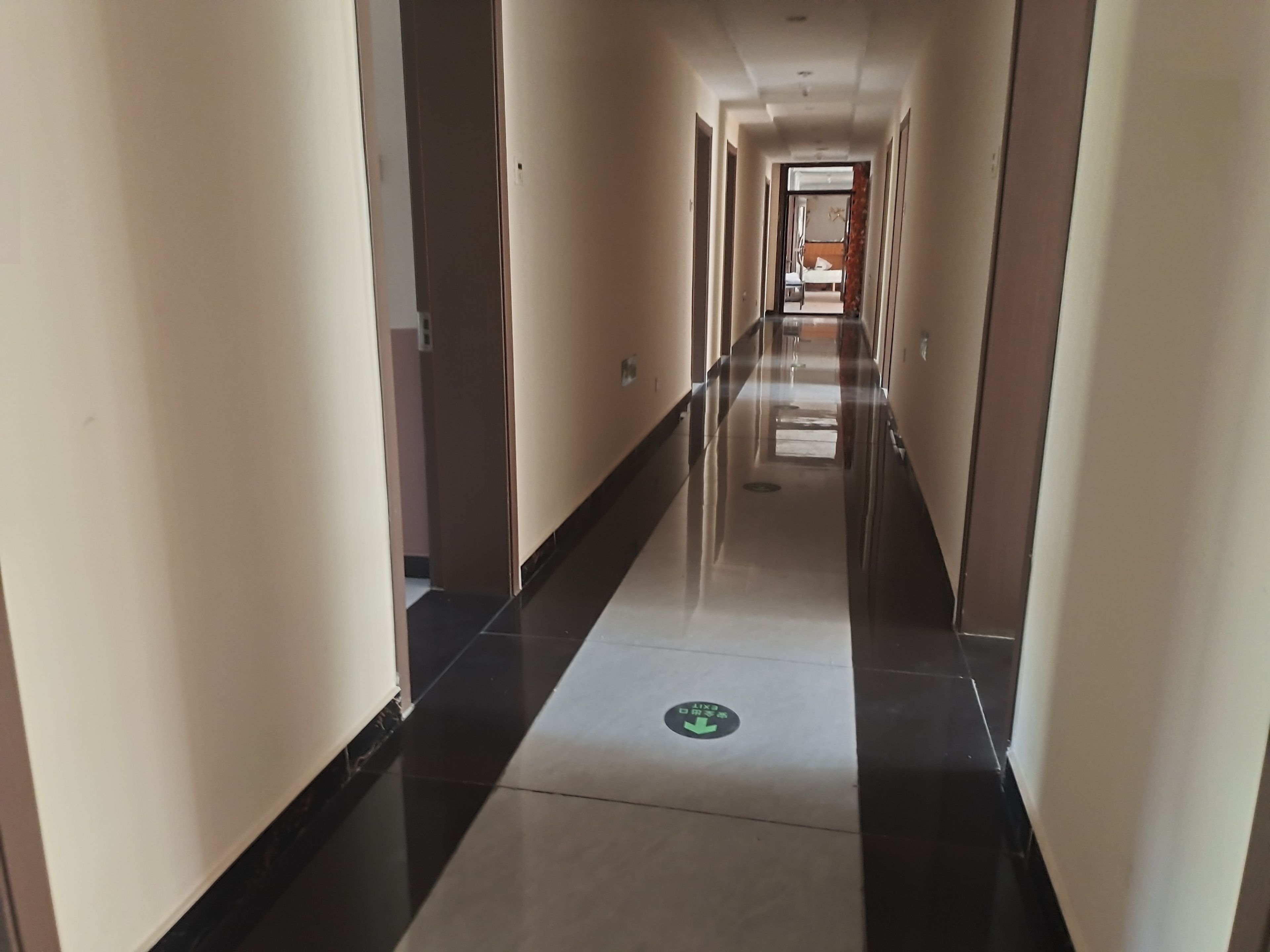 Een hotelgang met een zwart-wit betegelde vloer, deuren aan beide kanten en een groen vluchtroutebord.