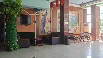 A lobby with a reception desk, seating area, decorative wall art, and a large potted plant.