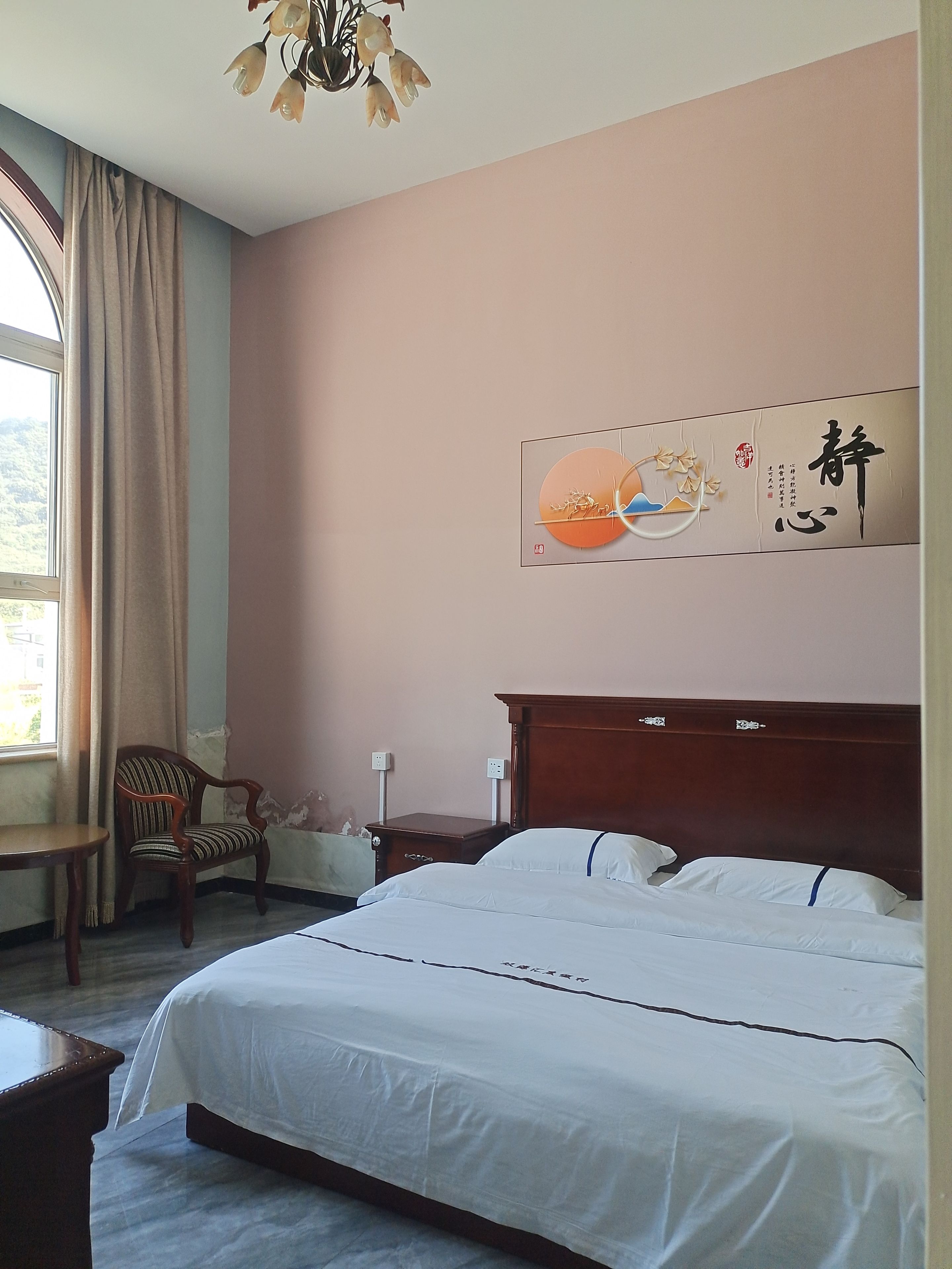A hotel room with a bed, a chair, a nightstand, and a wall with a decorative piece.