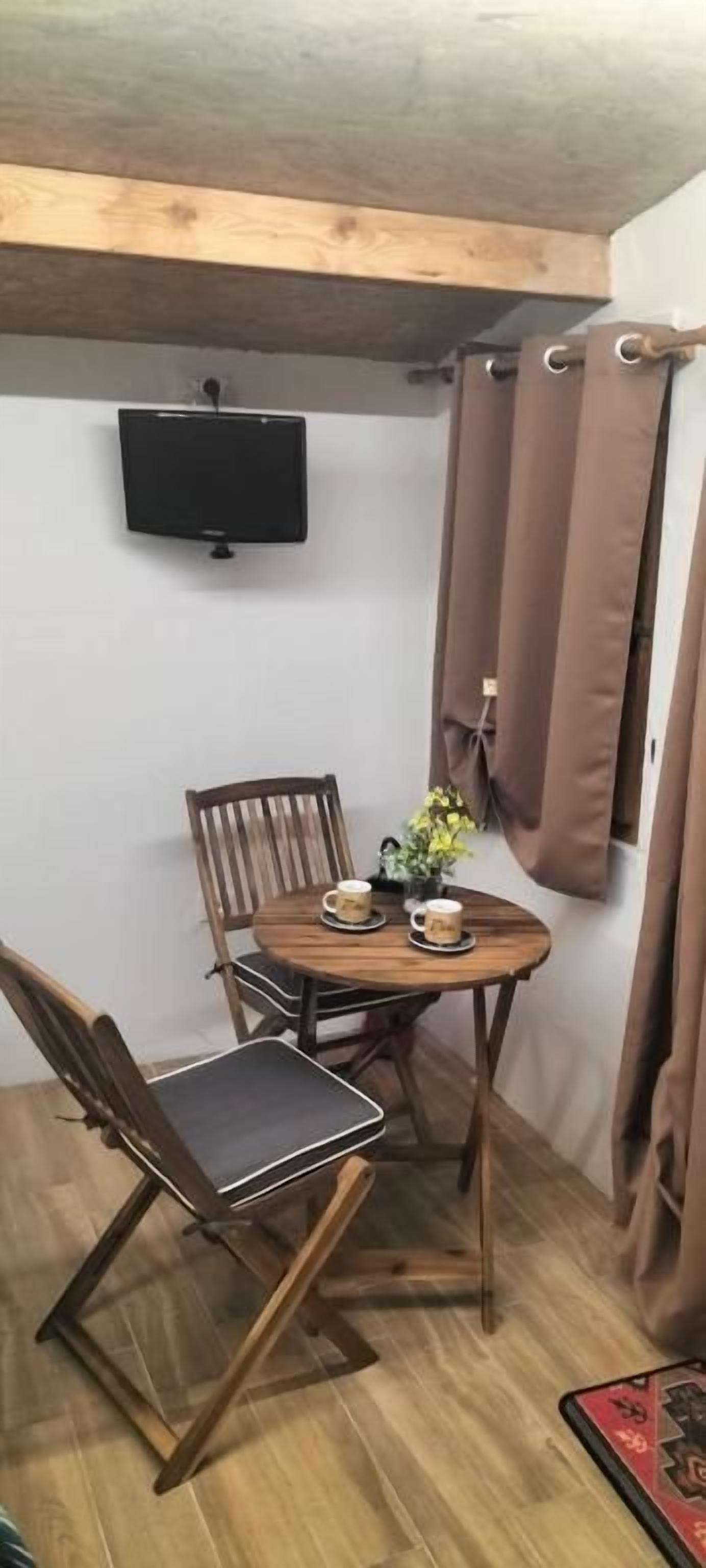 Una habitación de esquina con una mesa de madera, dos sillas, un televisor montado en la pared y cortinas marrones.
