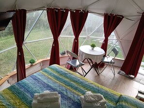 A tented room with a bed, a small table with chairs, and a view of the outdoors.