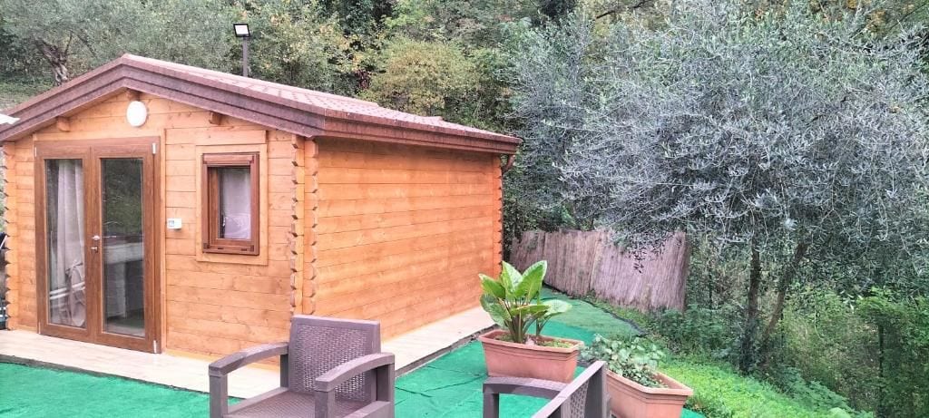 A wooden cabin with a sliding glass door, a small window, and a patio area with chairs and potted plants.