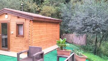 A wooden cabin with a sliding glass door, a small window, and a patio area with chairs and potted plants.