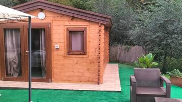 Eine Holzhütte mit einer Schiebetür aus Glas, einem kleinen Fenster und einer Terrasse mit einem Stuhl und einem Blumentopf.