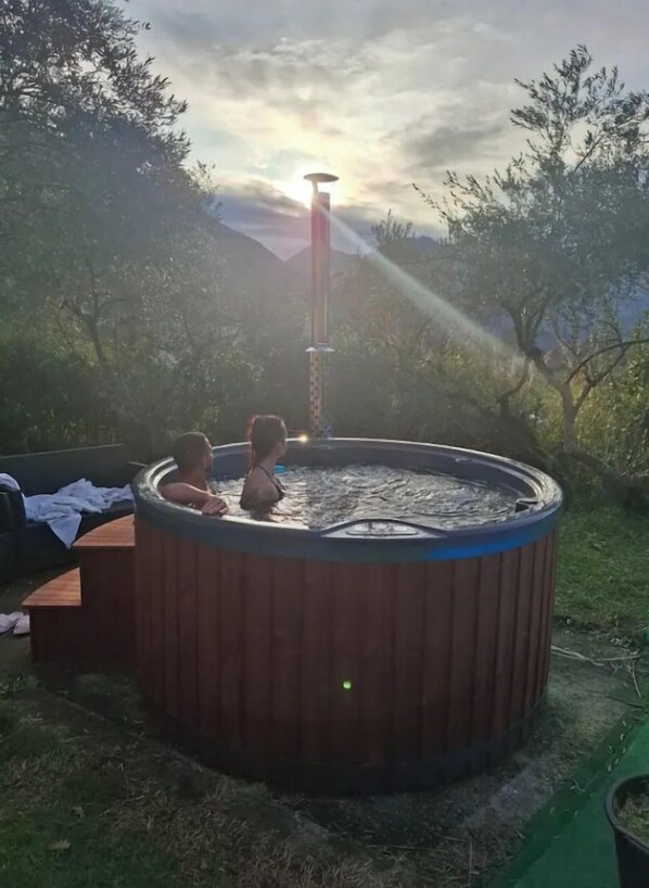 A hot tub outdoors with a wooden structure, surrounded by grass and trees.