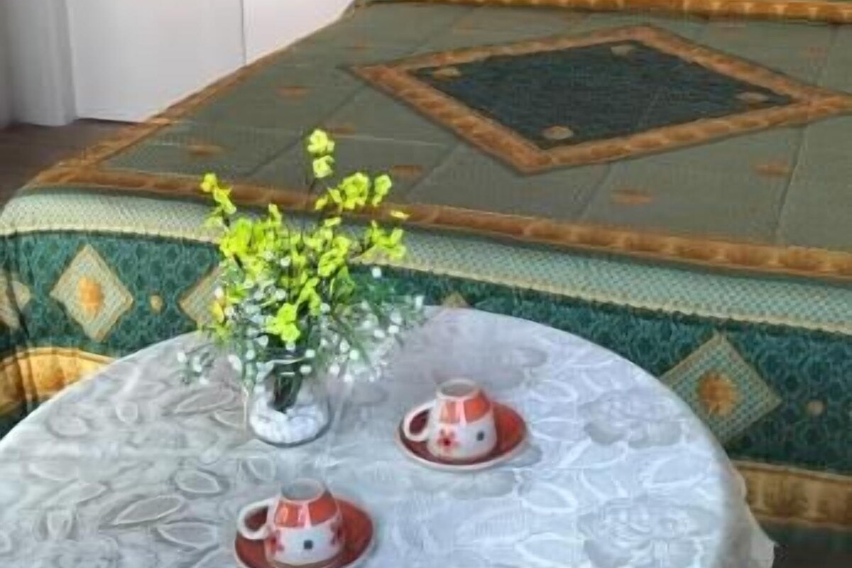 A room with a bed, a table with a lace tablecloth, and a vase with flowers.
