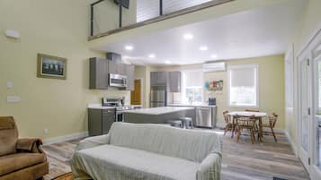Eine moderne Küche mit Edelstahlgeräten, ein Essbereich mit Holztisch und -stühlen sowie ein Wohnzimmer mit einer gepolsterten Couch.