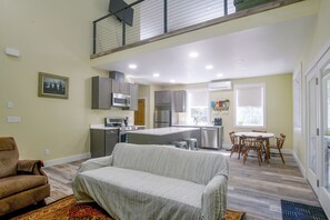 Eine moderne Küche mit Edelstahlgeräten, ein Essbereich mit Holztisch und -stühlen sowie ein Wohnzimmer mit einer gepolsterten Couch.