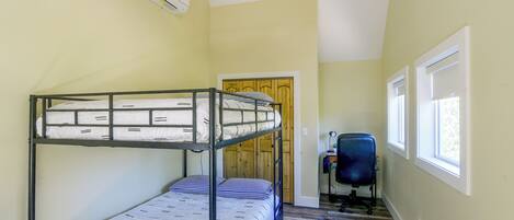 A bunk bed room with a desk and chair, a window, and an air conditioning unit.