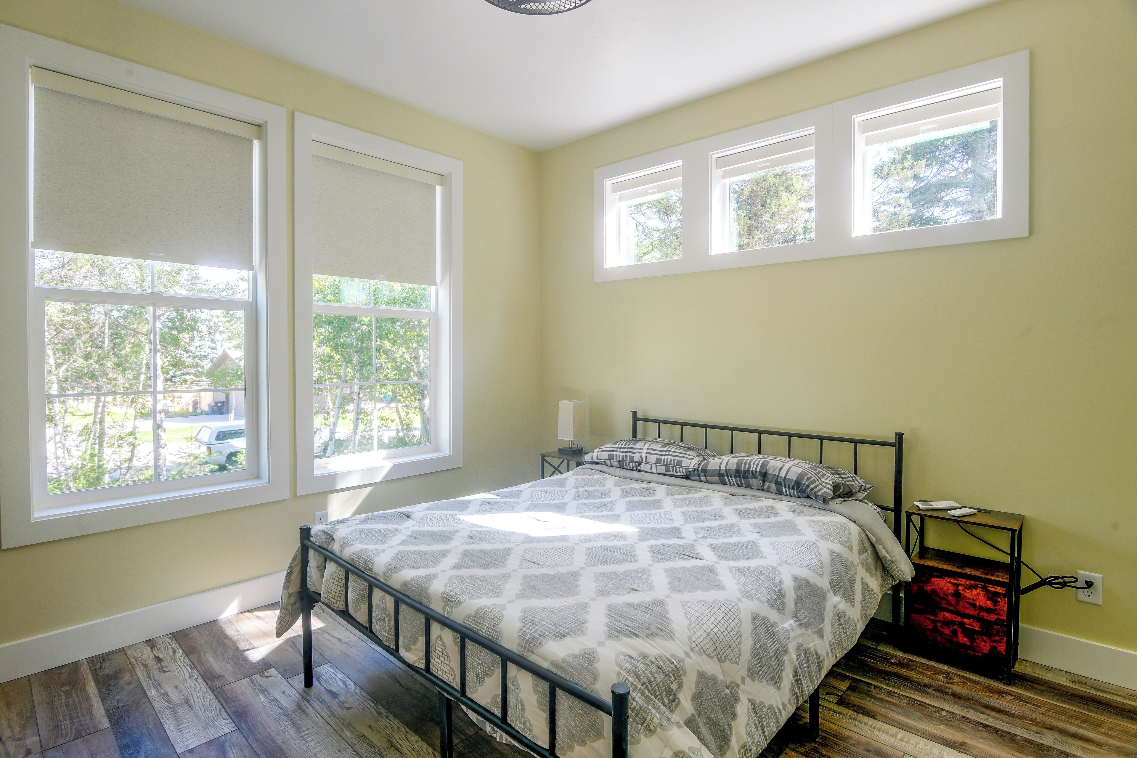 A bedroom with a bed, a nightstand, and a window with a view of trees.