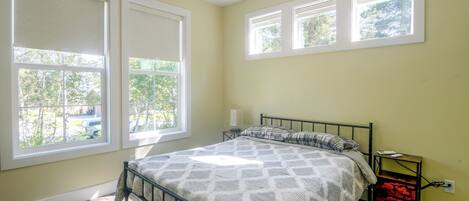 A bedroom with a bed, a nightstand, and a window with a view of trees.