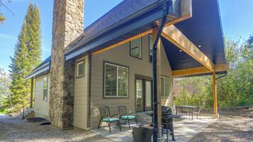 A two-story house with a stone chimney, large windows, and a covered patio area with outdoor furniture.
