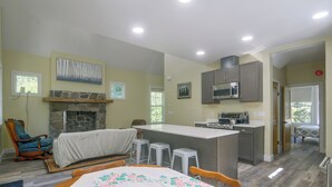 A spacious living area with a fireplace, a dining table with a floral tablecloth, a kitchen with modern appliances, and a view of the outdoors through windows. - Star Valley Retreat in Alpine Near Snake River (Alpine)