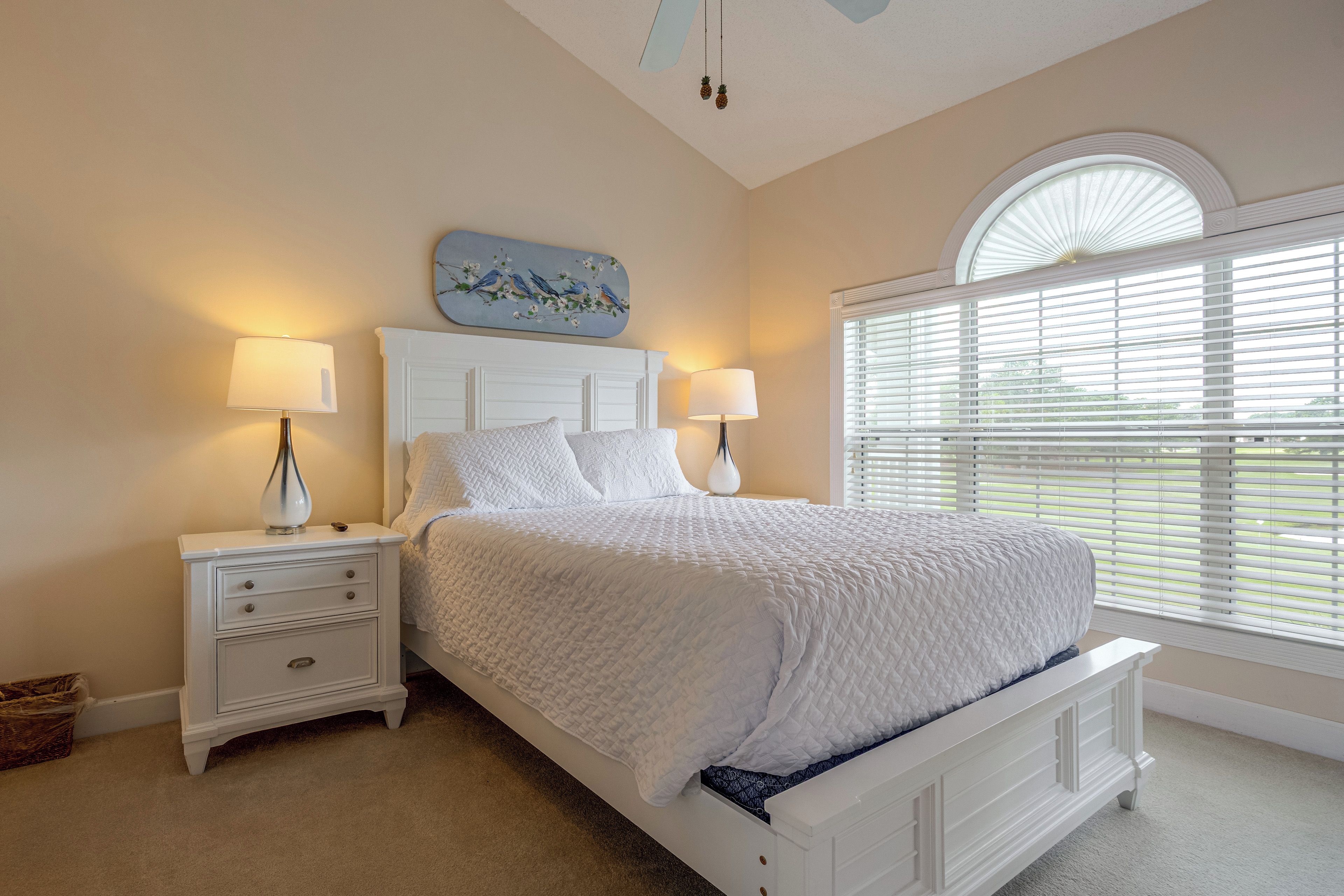 A bedroom with a bed, nightstands, a wall clock, and a window with blinds.