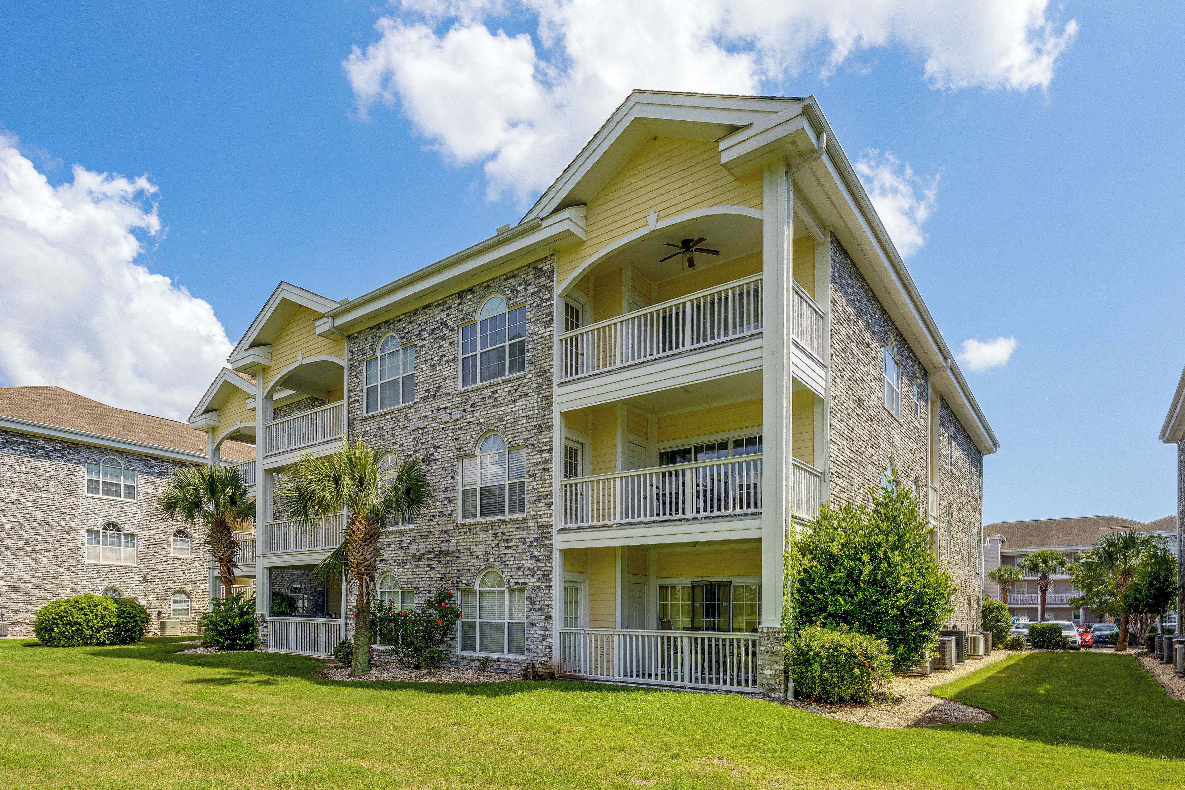 A multi-story building with a stone facade, balconies, and a well-maintained lawn.
