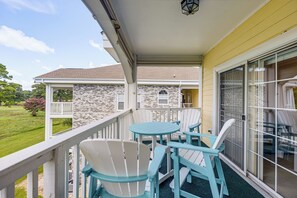 A balcony with a table and chairs, a stone wall, and a view of a grassy area. - Birdies, Beaches & Boardwalks: Myrtle Beach Gem! (Myrtle Beach)