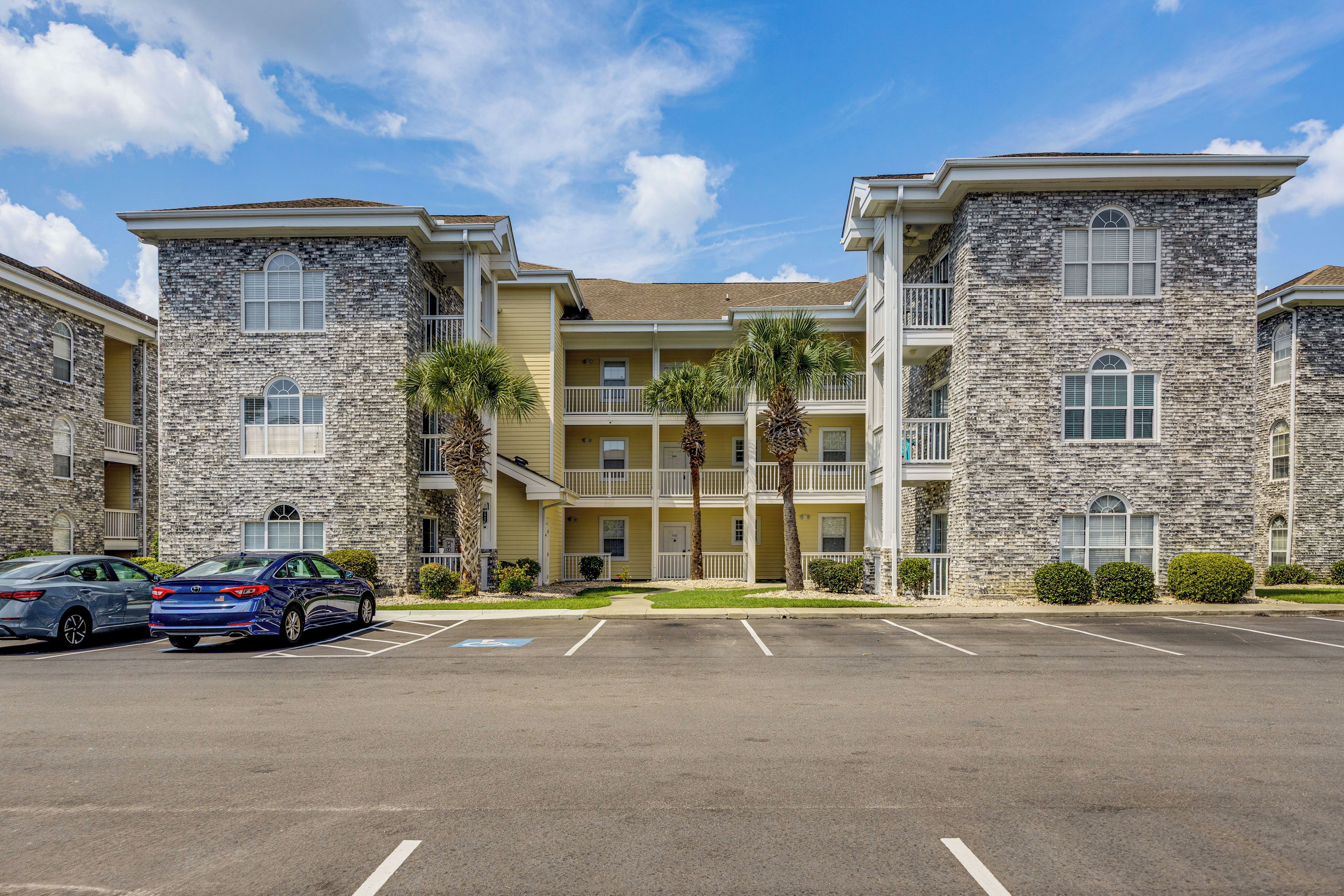 A multi-story building with a stone facade, a parking lot, and a clear sky.