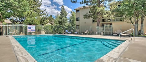 A rectangular swimming pool with clear blue water, surrounded by a metal fence and trees.