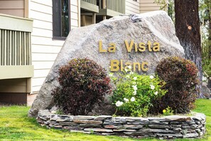 A large stone sign with 'La Vista Blanche' engraved on it, surrounded by a stone wall and small bushes with red and white flowers. - Walkable Condo Near Ski Shuttle & Mammoth Creek! (Mammoth Lakes)