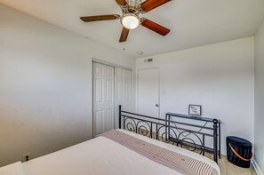 A bedroom with a bed, a ceiling fan, a door, a small table, and a trash bin. - 5 Mi to Empire Polo Club! Poolside Group Getaway (Indio)