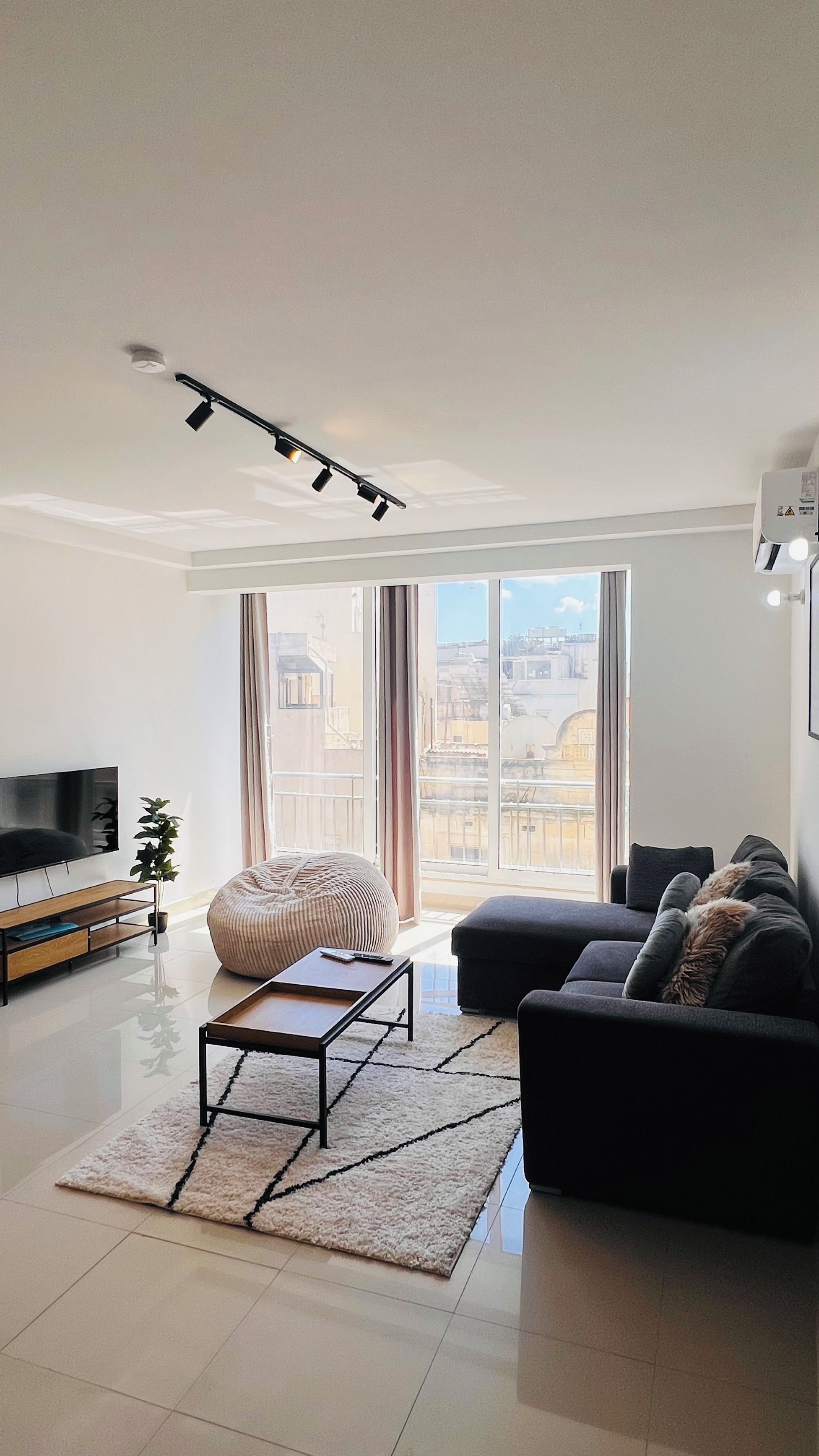 A modern living room with a sofa, a bean bag, a coffee table, and a TV.
