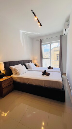 Une chambre d’hôtel avec un grand lit, deux tables de chevet, une fenêtre avec des rideaux et un luminaire au plafond.