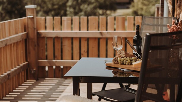 Un terrazzo in legno con tavolo e sedie, una bottiglia di vino e un bicchiere.