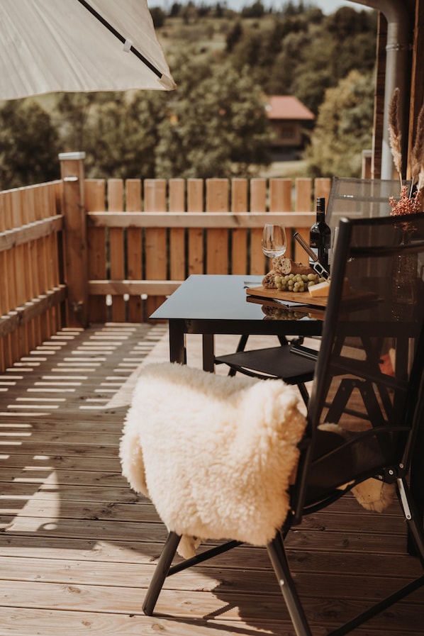 Eine Holzterrasse mit Tisch und Stühlen, einer Weinflasche und einem Glas.