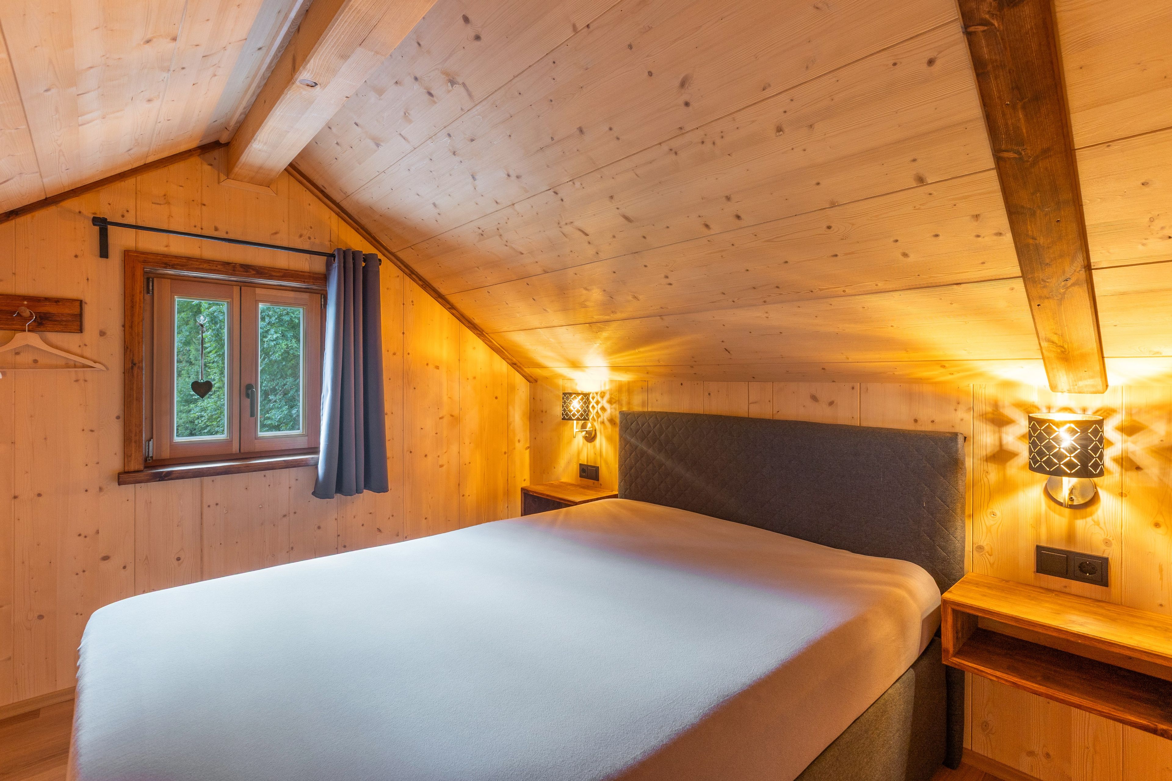 Ein Zimmer mit Holzboden, einem Bett, einem Fenster mit Vorhängen und Wandleuchten.