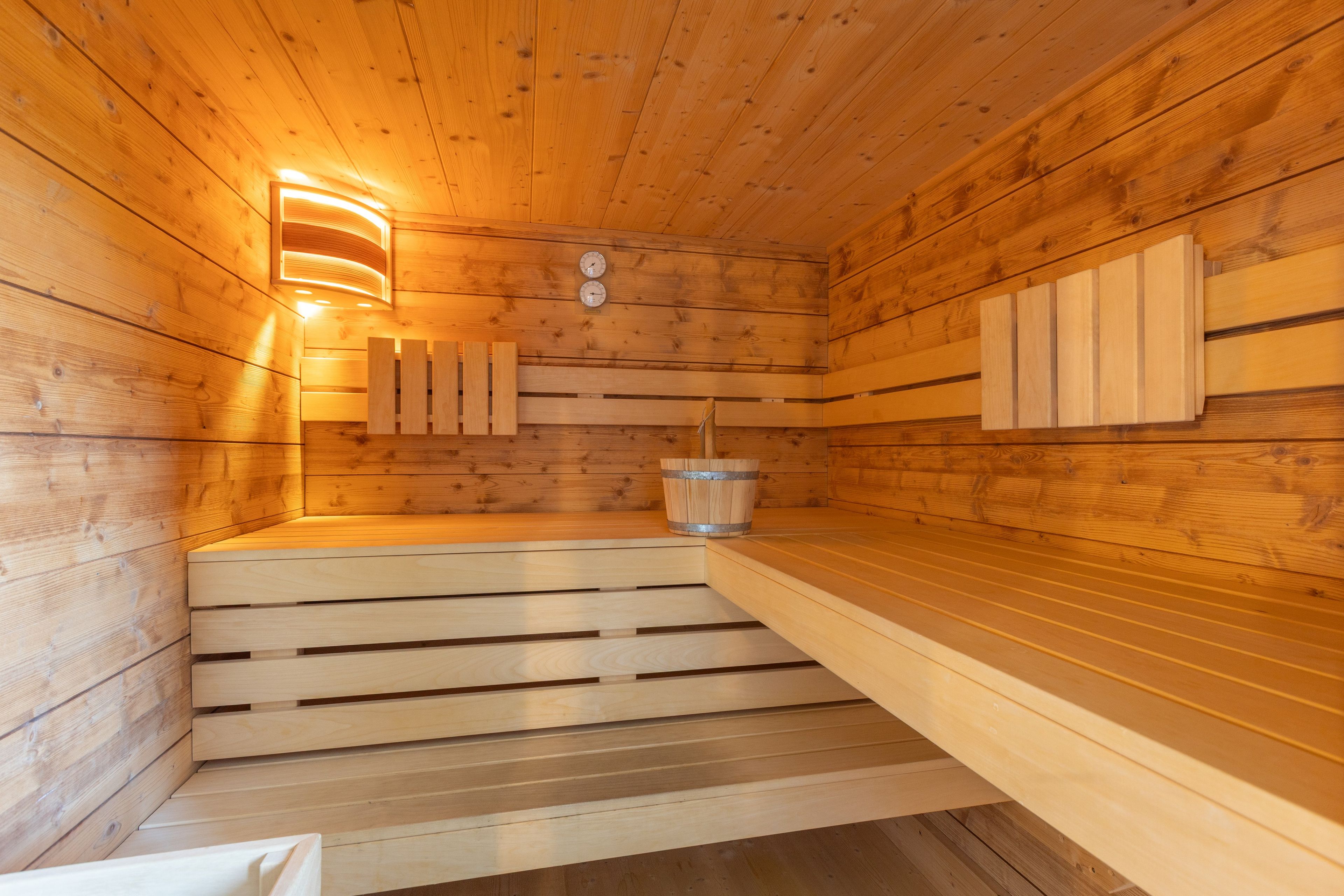 A sauna with wooden walls and benches, a wall-mounted heater, and a bucket.