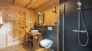 Une salle de bain intérieure au décor en bois, équipée de toilettes, d’un lavabo et d’une douche.