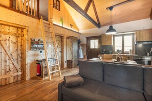 A wooden interior with a sofa, a ladder, and a kitchen area. - Chalet “Oberwald 1” with Private Terrace, Garden, Sauna, Wi-Fi, and Parking (Schotten)