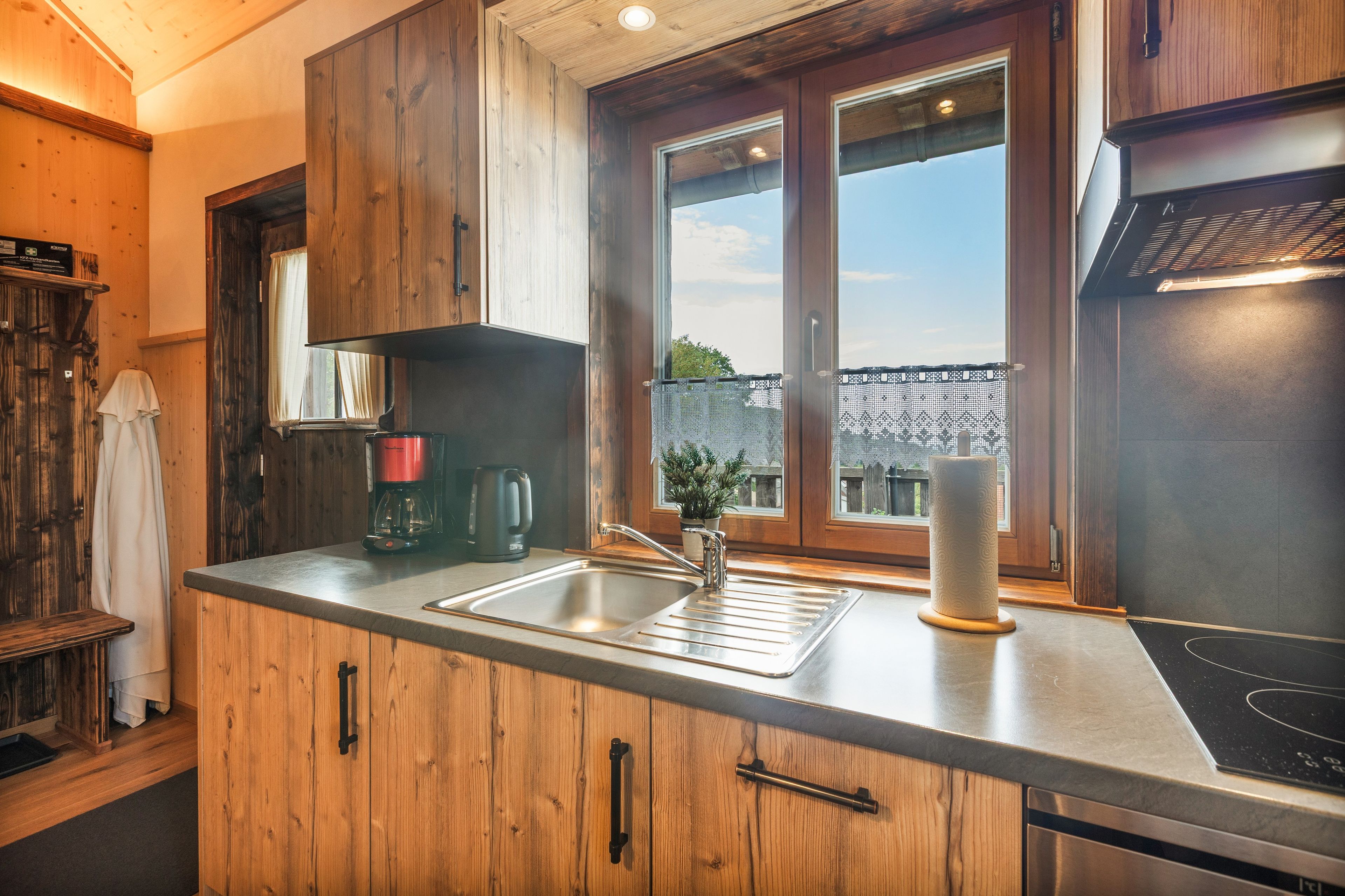 Eine Küche mit Holzschränken, einer Edelstahl-Spüle, einer Kaffeemaschine und einem Fenster mit Aussicht.