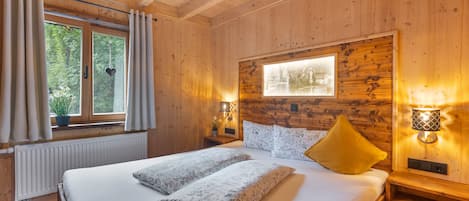A wooden room with a bed, two bedside tables, a window with curtains, and a wall-mounted picture.