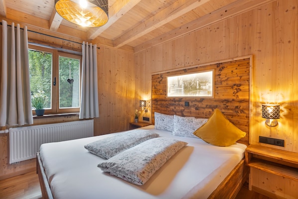 Une pièce en bois avec un lit, deux tables de chevet, une fenêtre avec des rideaux et un tableau accroché au mur.