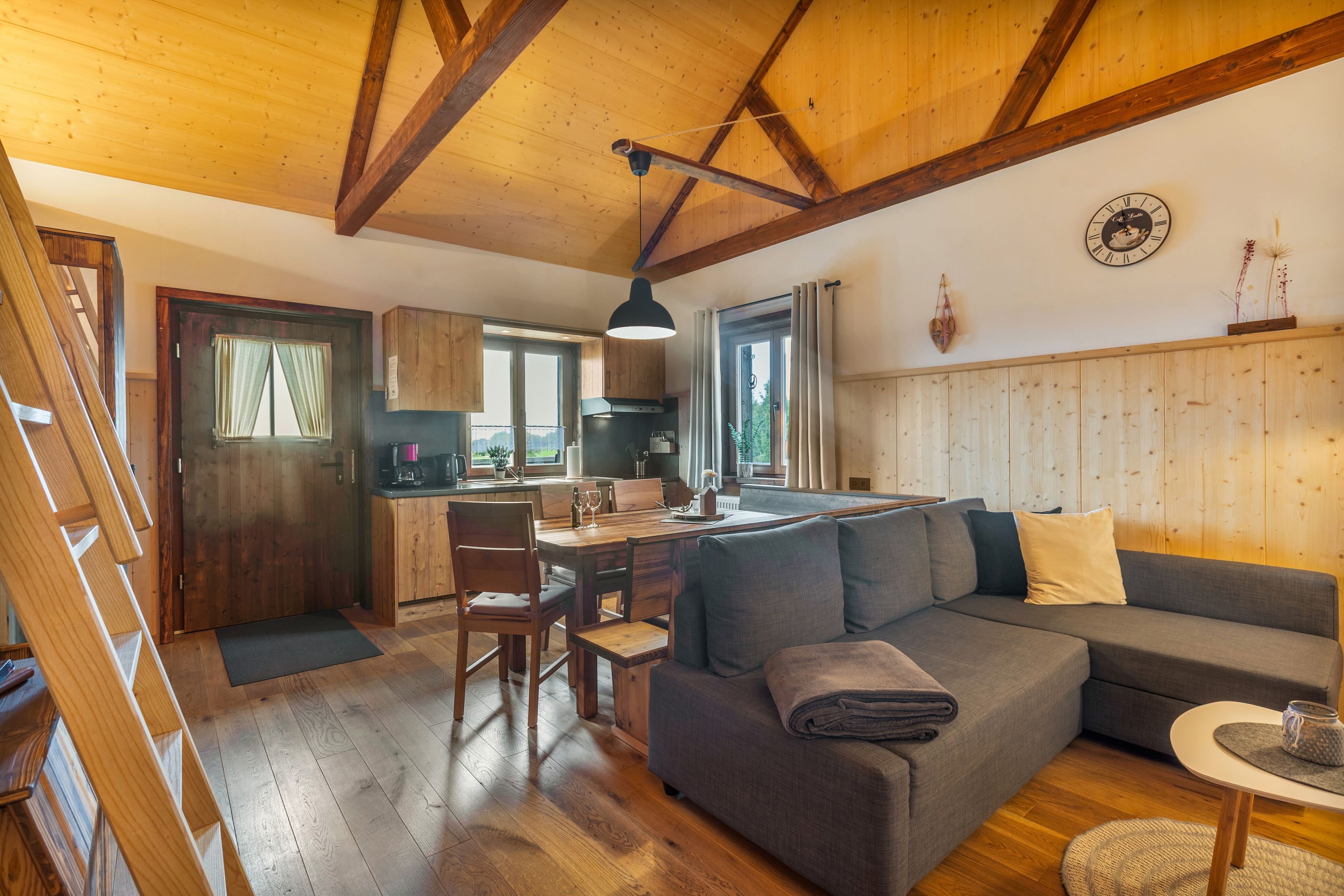 Un salón acogedor con techo de madera, un sofá, una mesa de comedor y una cocina al fondo.