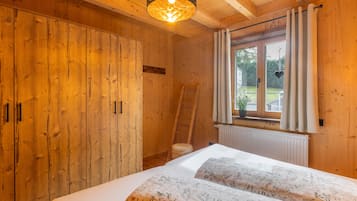 A wooden room with a bed, a wardrobe, a window with curtains, and a ladder.