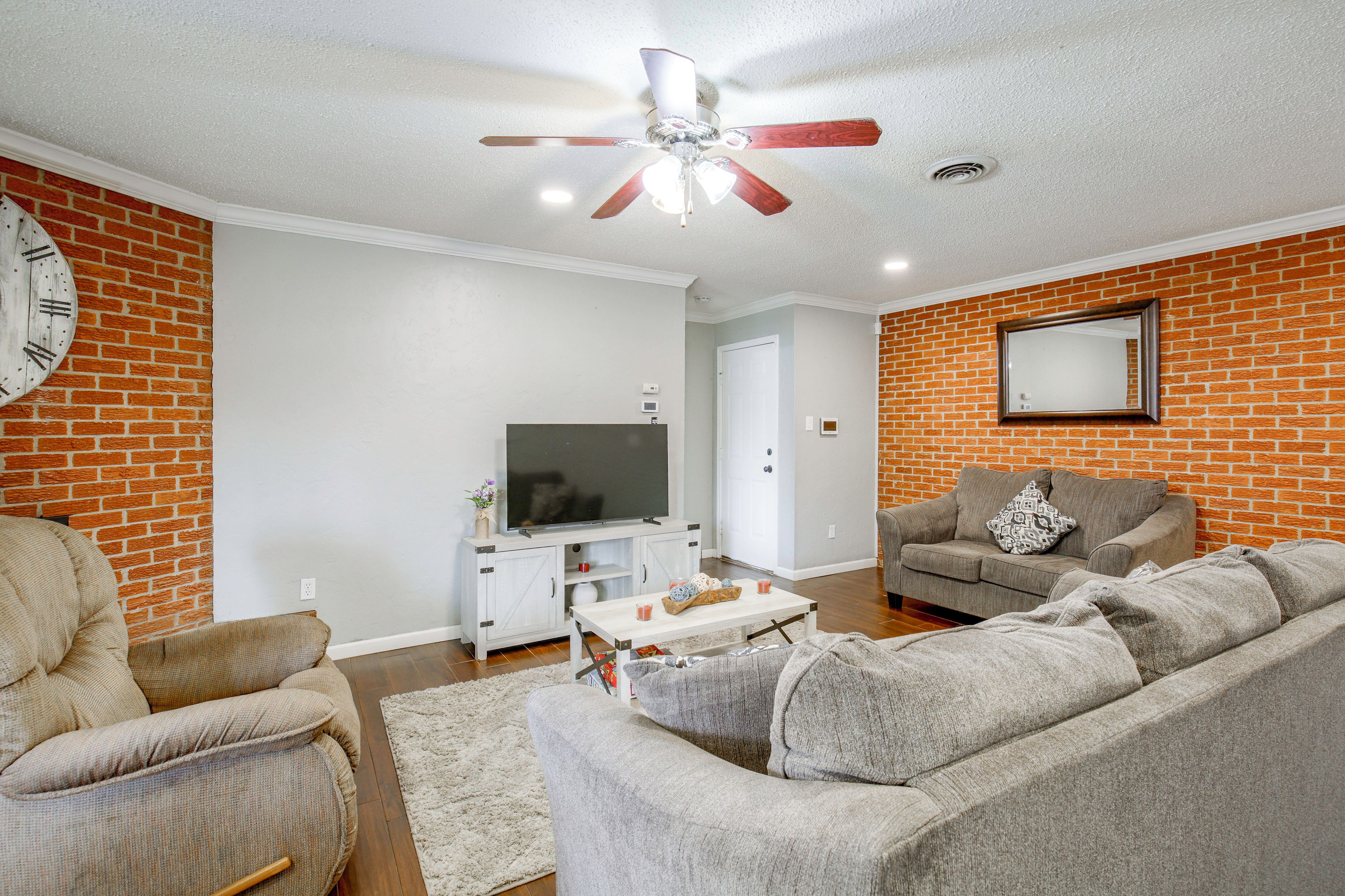 A living room with a brick wall, a ceiling fan, a flat-screen TV, and a grey sofa.