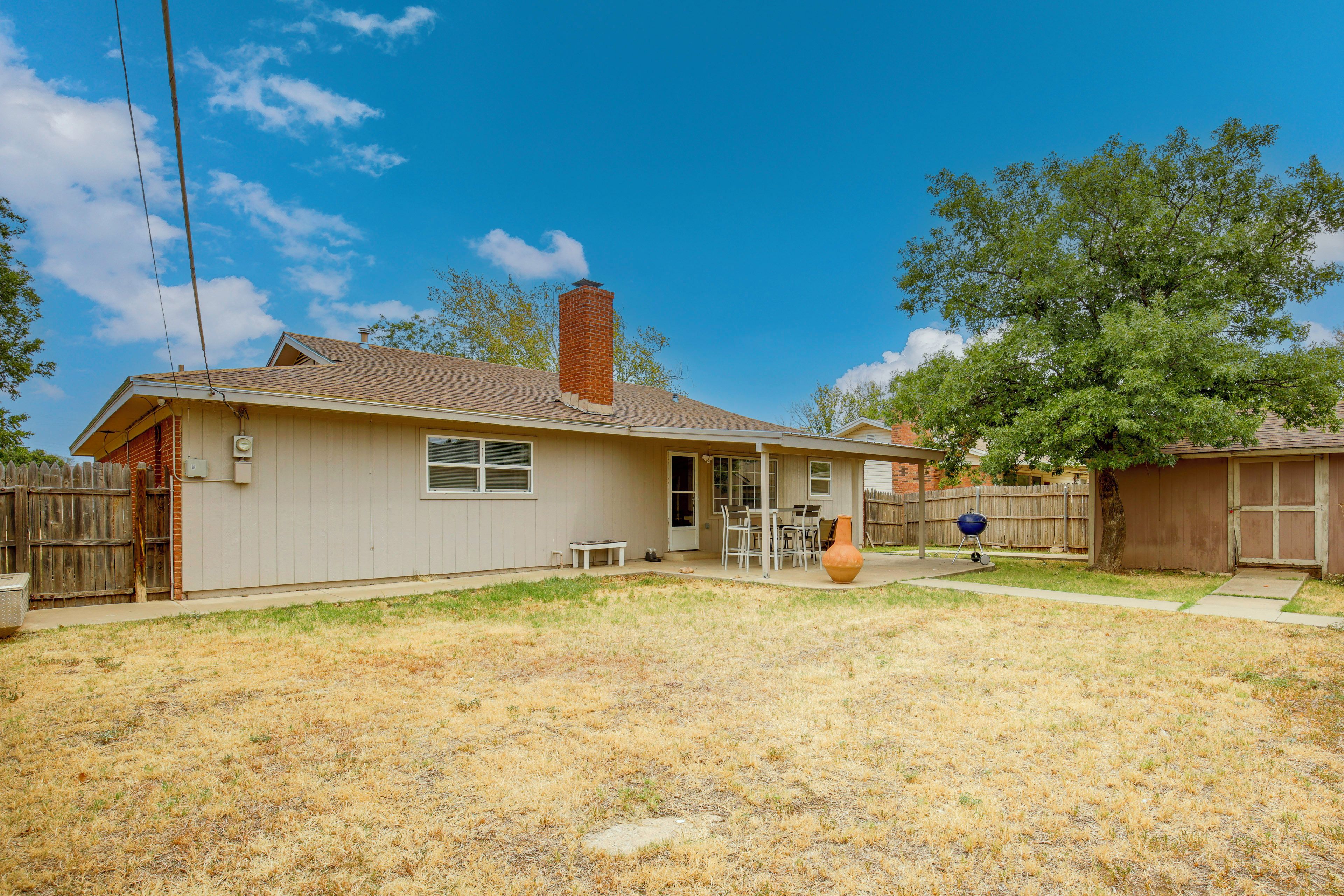 A residential house with a chimney, a patio with a table and chairs, and a fenced yard.