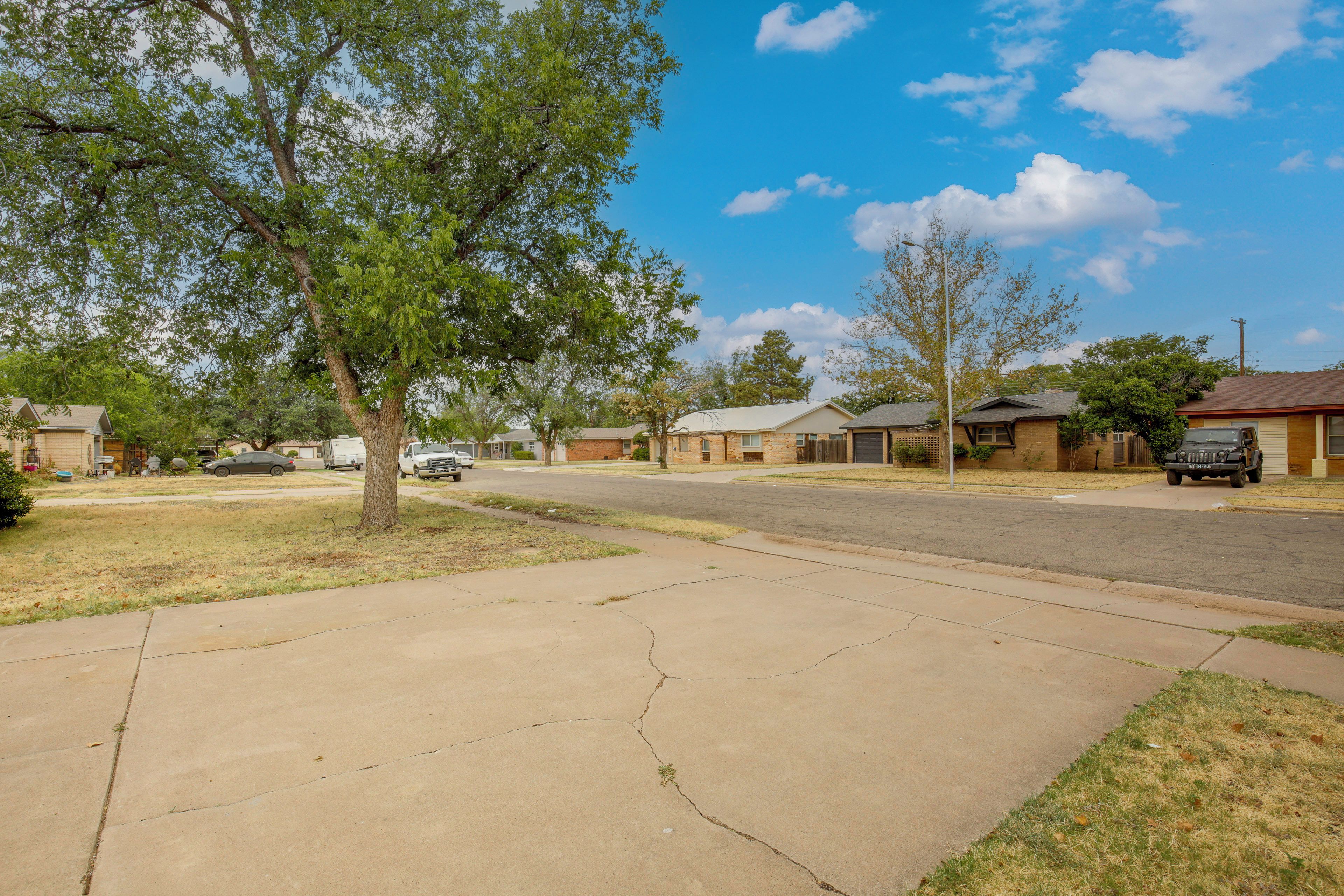 A residential street with houses, a sidewalk, and a tree.