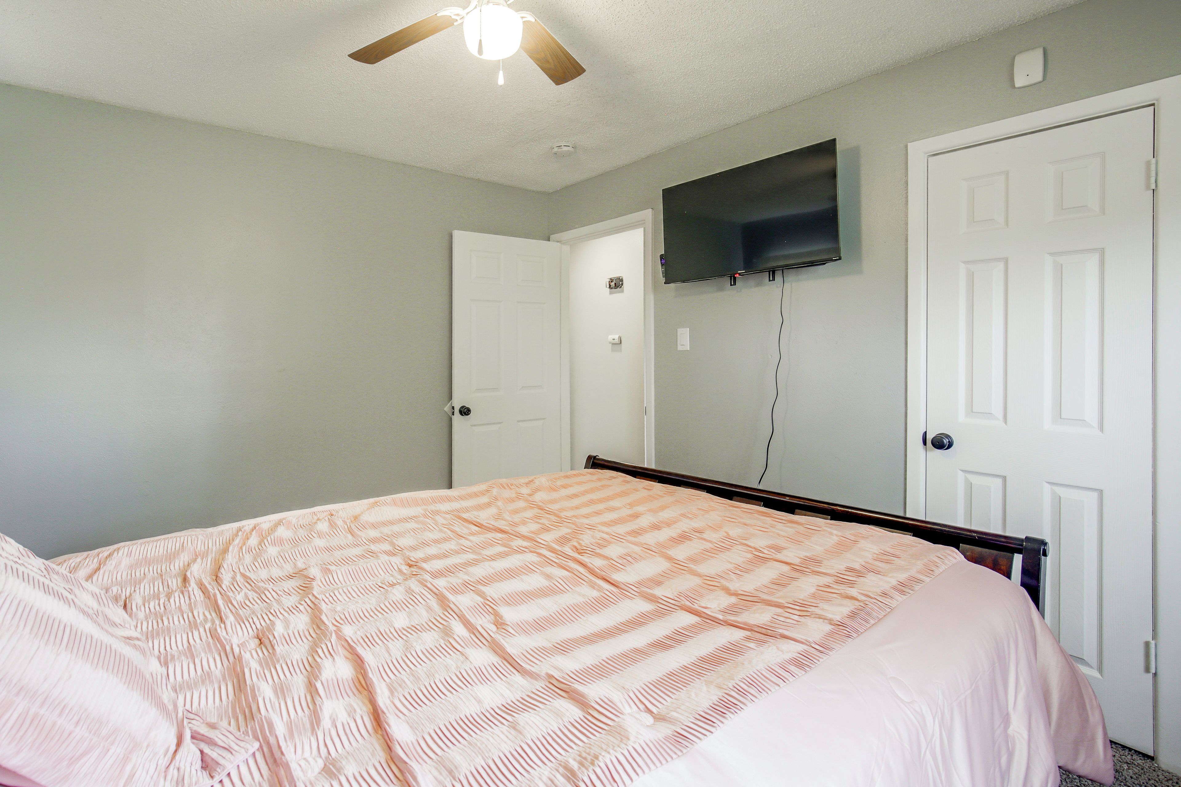 Un dormitorio con una cama, ventilador de techo, televisor montado y dos puertas.
