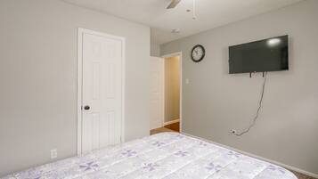 A bedroom with a bed, a door, a ceiling fan, a wall-mounted TV, and a clock.