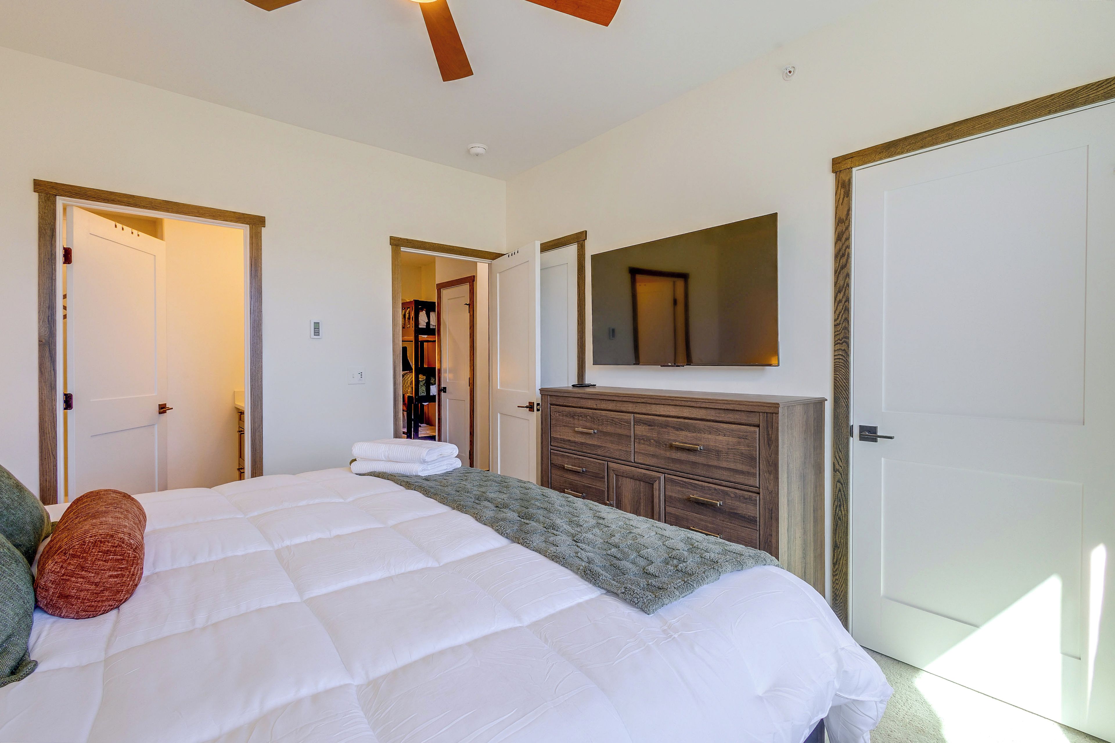 A bedroom with a large bed, a dresser, a mirror, and two doors.