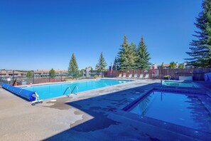 A swimming pool with a wooden deck, lounge chairs, and a fenced area with trees. - Ski, Bike & Explore Winter Park! Modern Condo (Fraser)