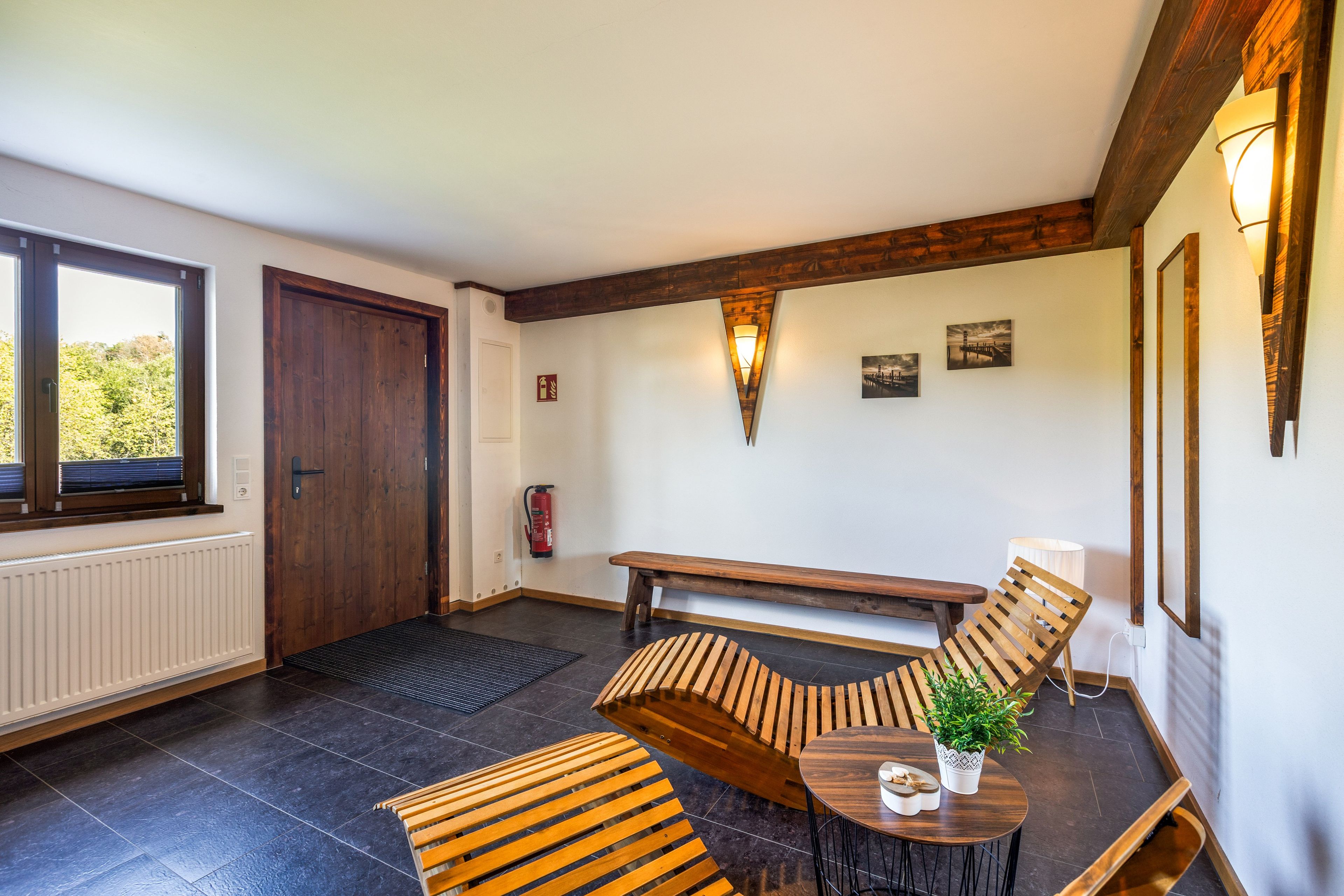 A room with a wooden bench, a round table with a potted plant, and a fire extinguisher mounted on the wall.