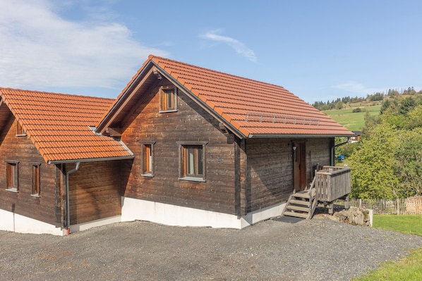 A wooden house with a sloped roof and a gravel driveway.